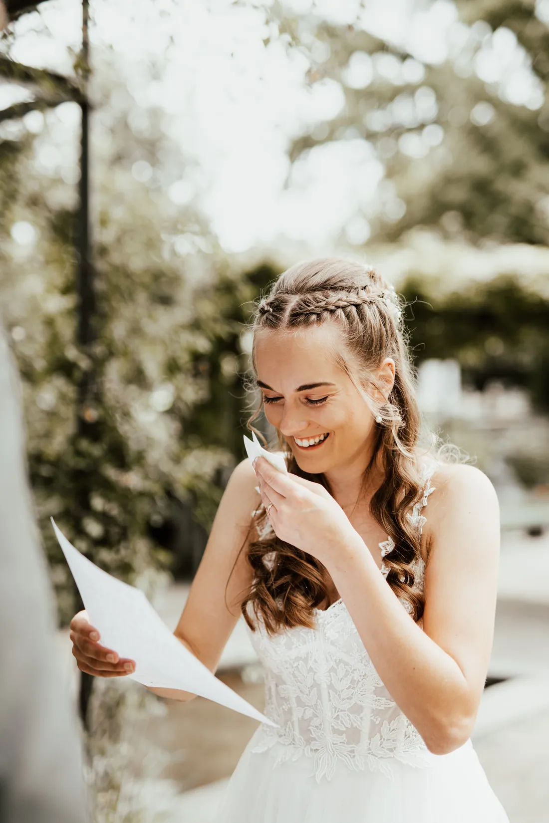 Braut mit geflochtenem Haar lacht beim Lesen eines Briefs