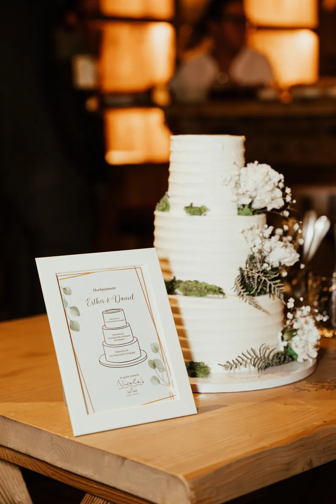 Hochzeitstorte mit weissen Blumen neben einer Menükarte