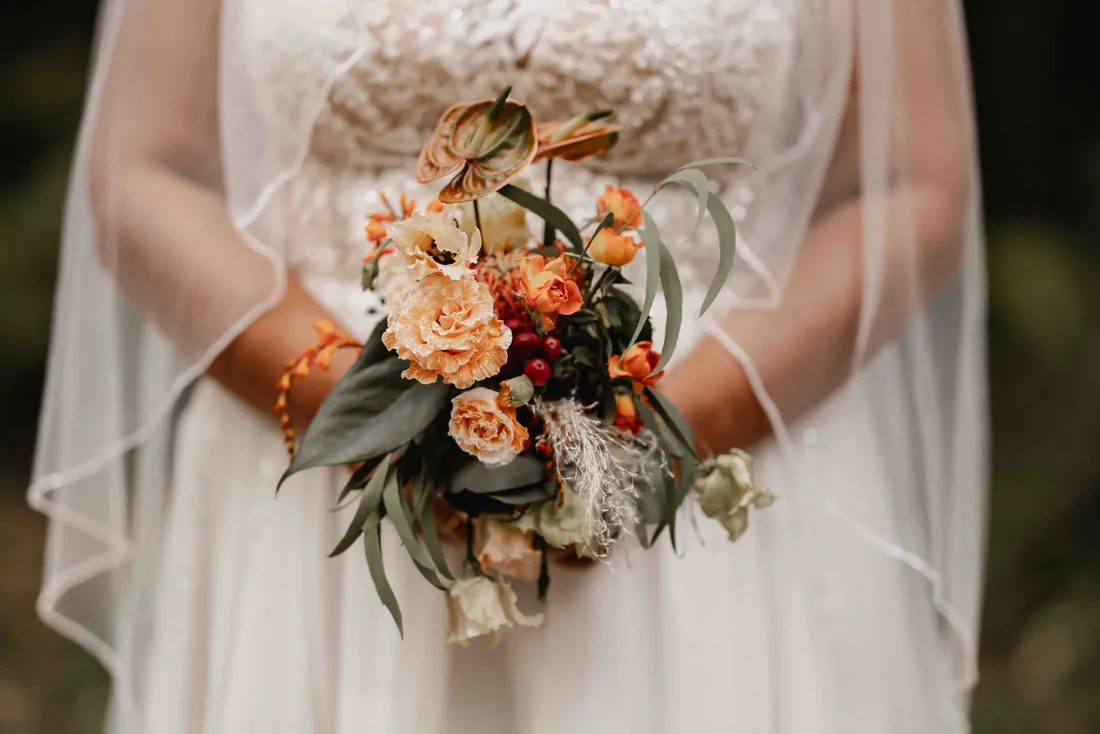 Brautstrauss mit orangen und rosa Blüten vor dem Kleid