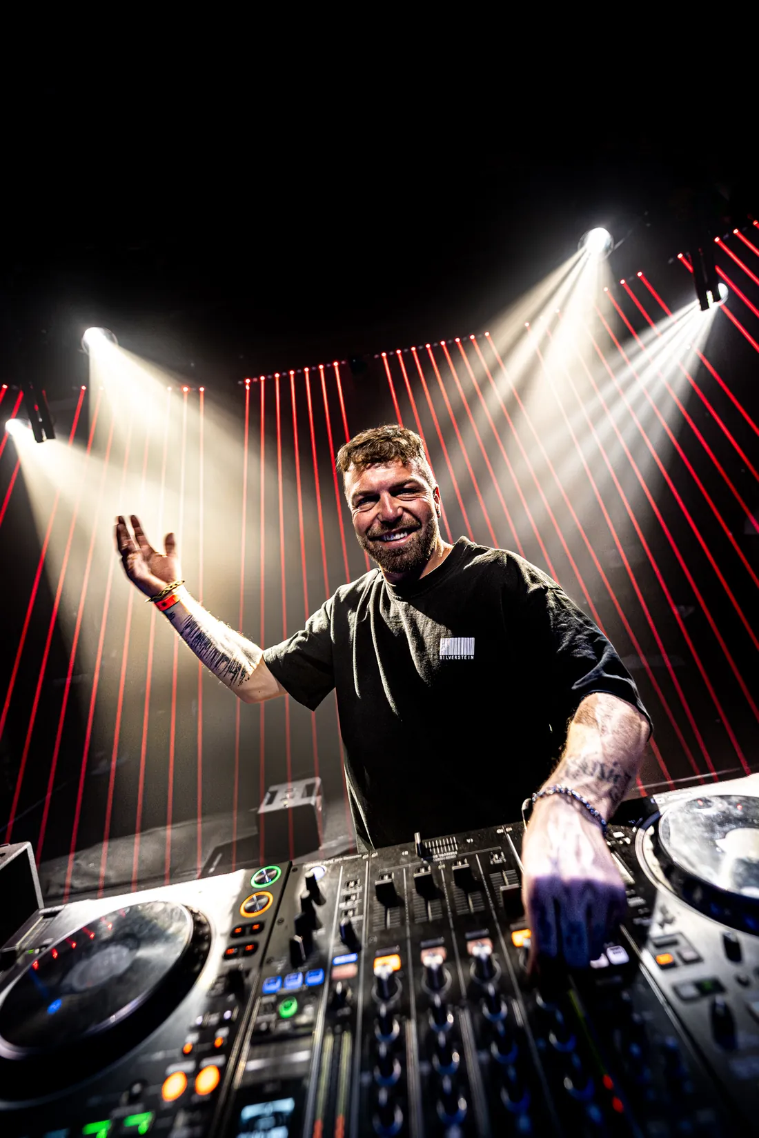 DJ mit ausgestrecktem Arm unter Scheinwerfern