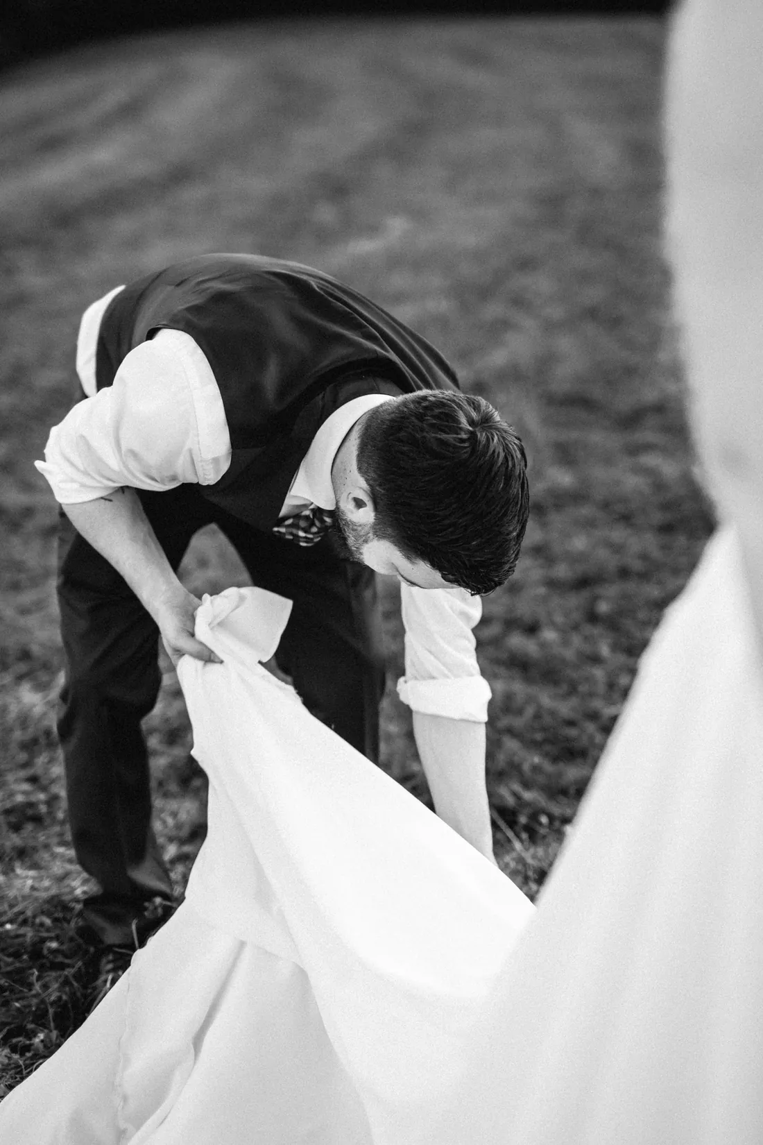 Bräutigam bückt sich und richtet das Kleid der Braut, Schwarzweiss