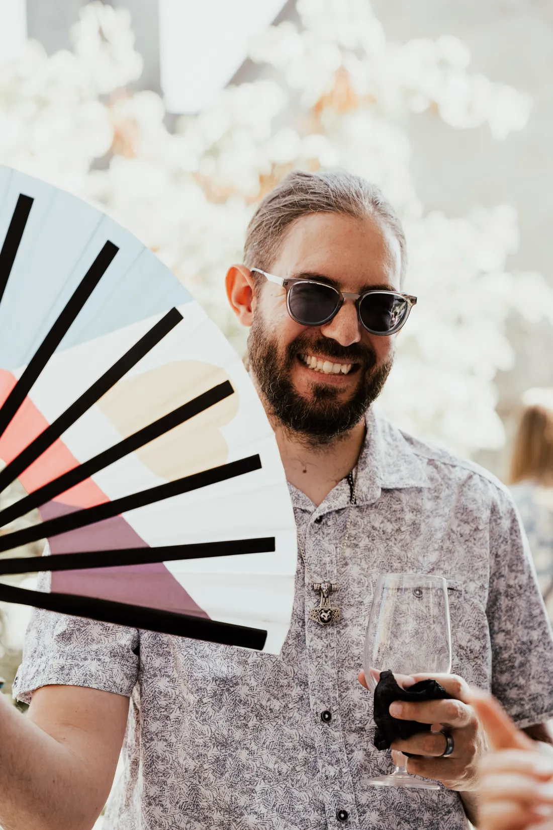 Hochzeitsgast mit Sonnenbrille und Fächer lacht beim Apéro
