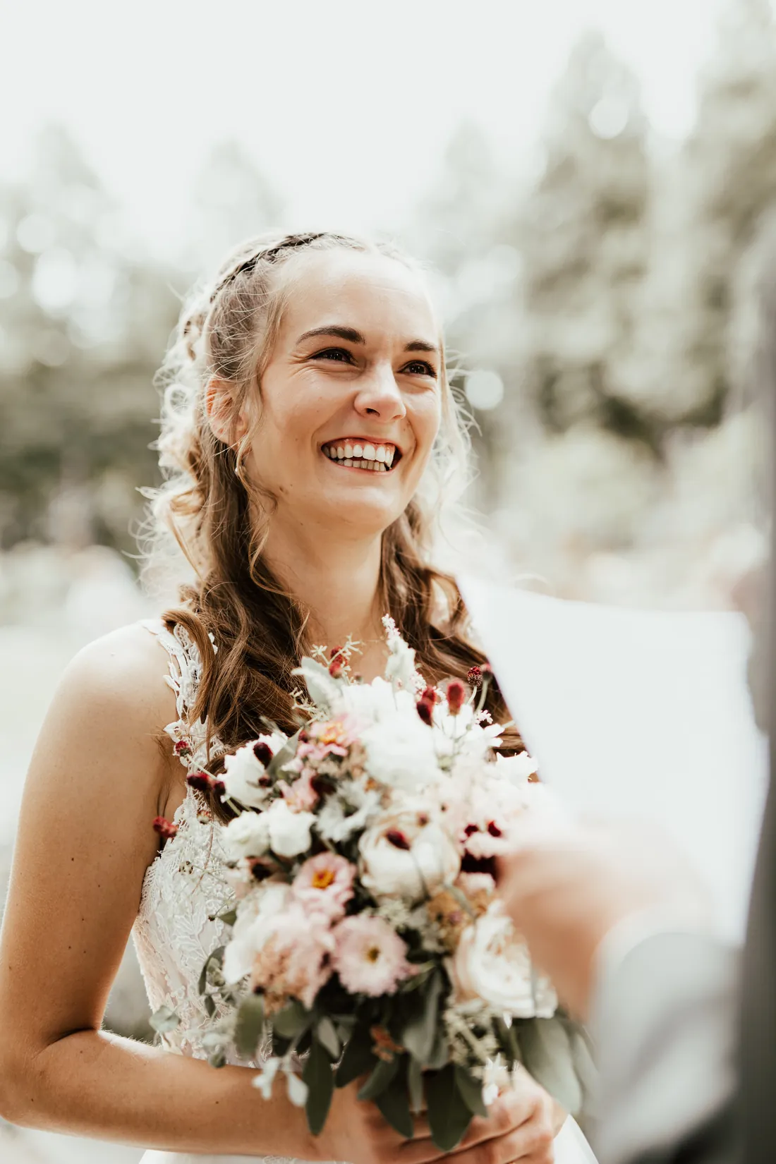 Braut lacht mit Blumenstrauss und Haarschmuck